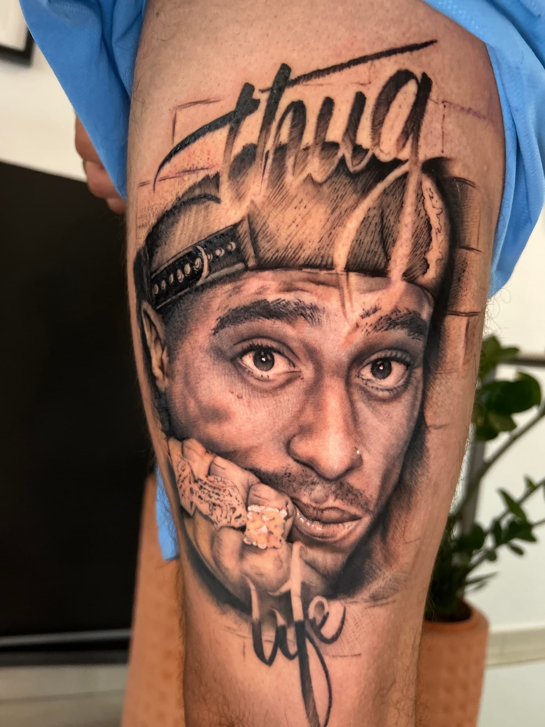 Black and grey portrait in a backwards cap, a ringed hand at the chin and “Thug Life” in script, on the thigh.