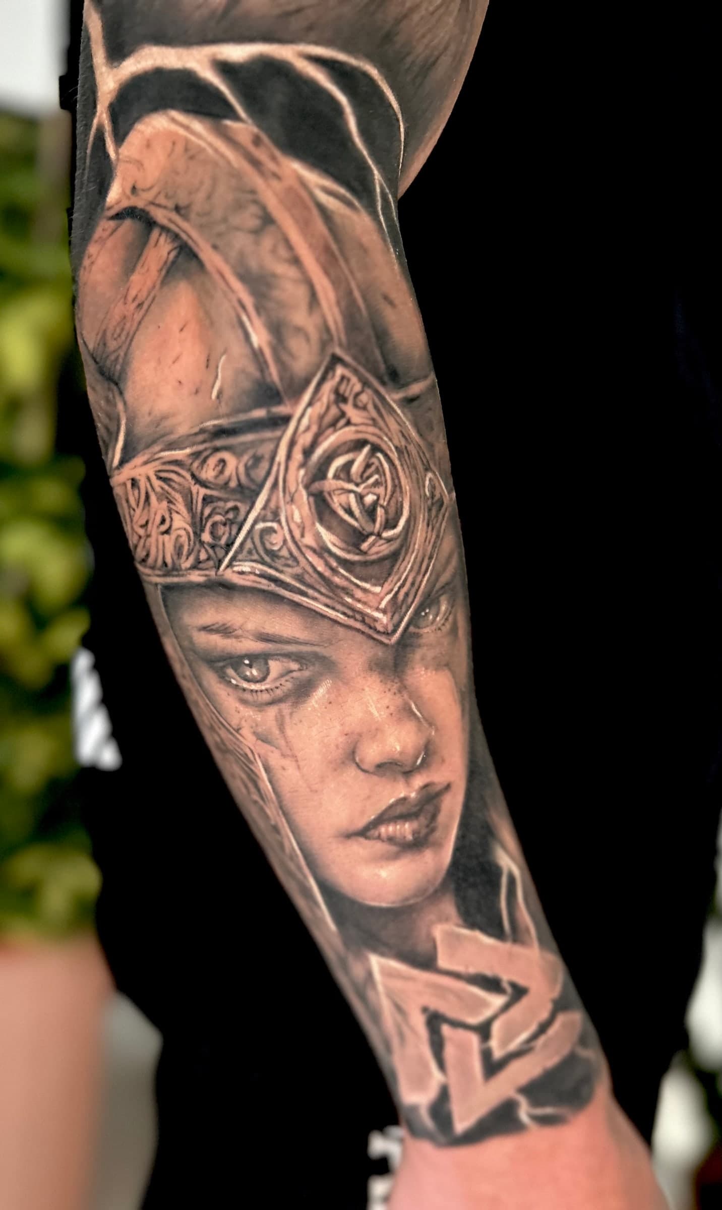 Black and grey Valkyrie in an ornate helmet above a valknut symbol, on the forearm.