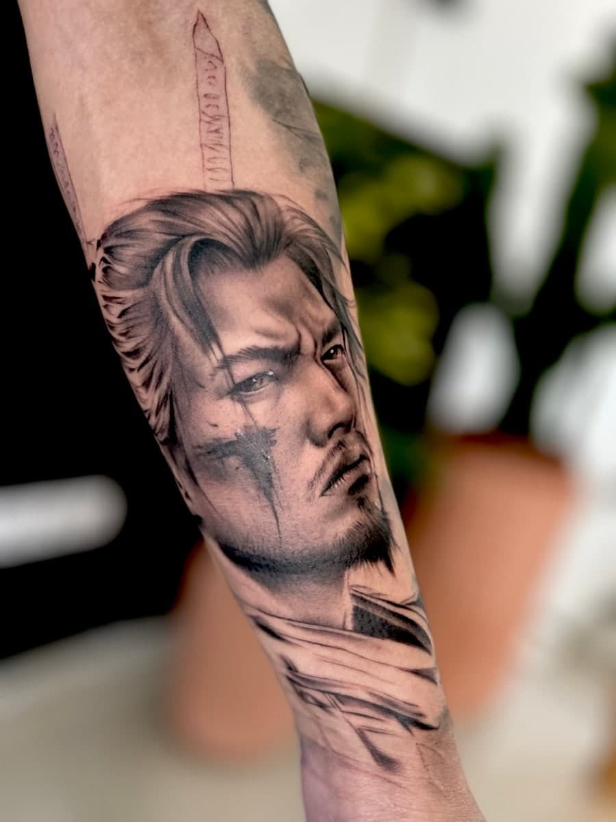 Black and grey portrait of a long-haired warrior with a sword rising behind, on the forearm.